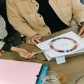 Two people reviewing a color wheel chart at a table, with a pink folder and glass jar nearby