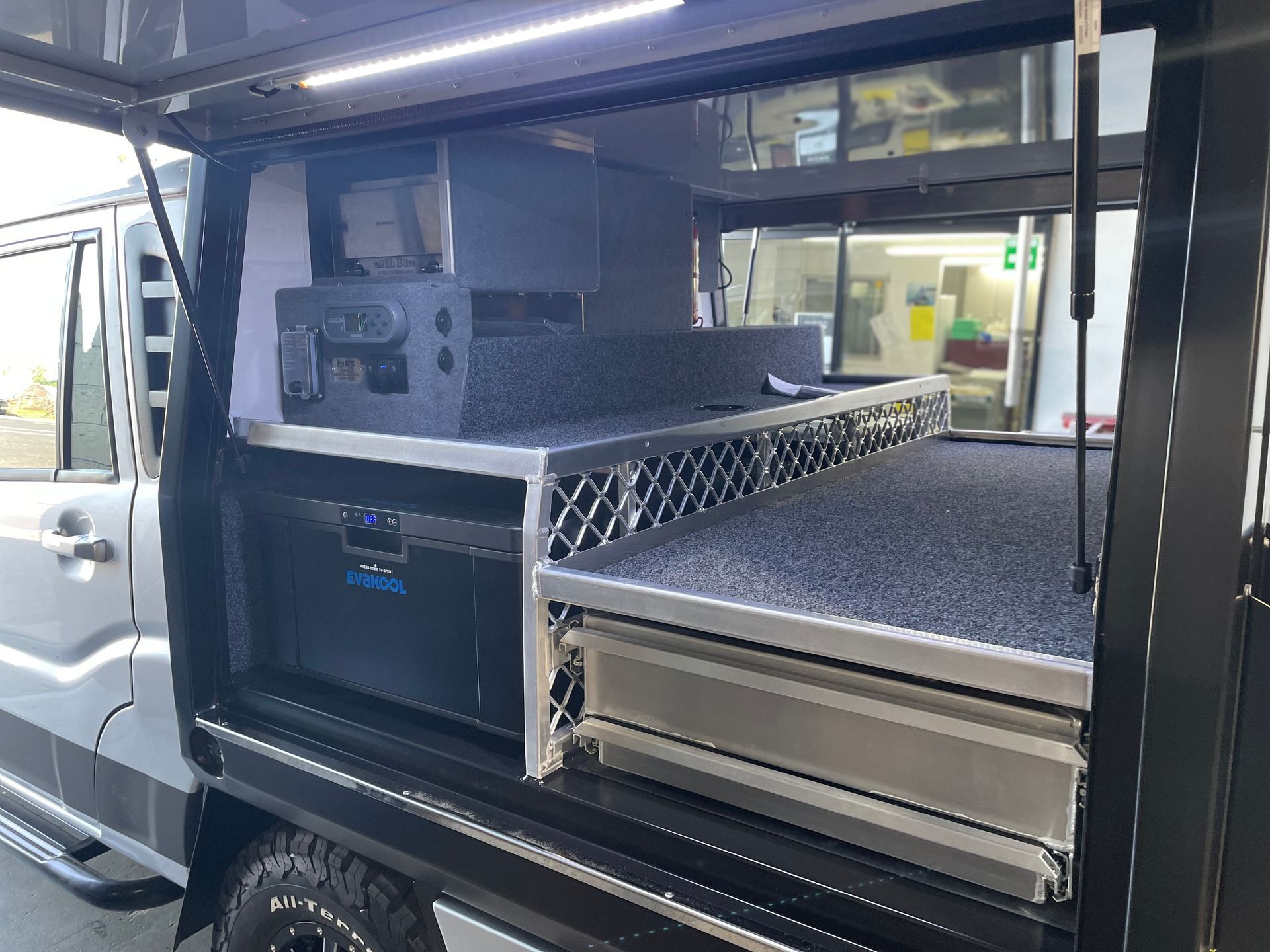 Inside a utility vehicle, a custom storage setup with a fridge, drawers, and a black countertop.— Boyd's Fabrications In Portsmith, QLD 