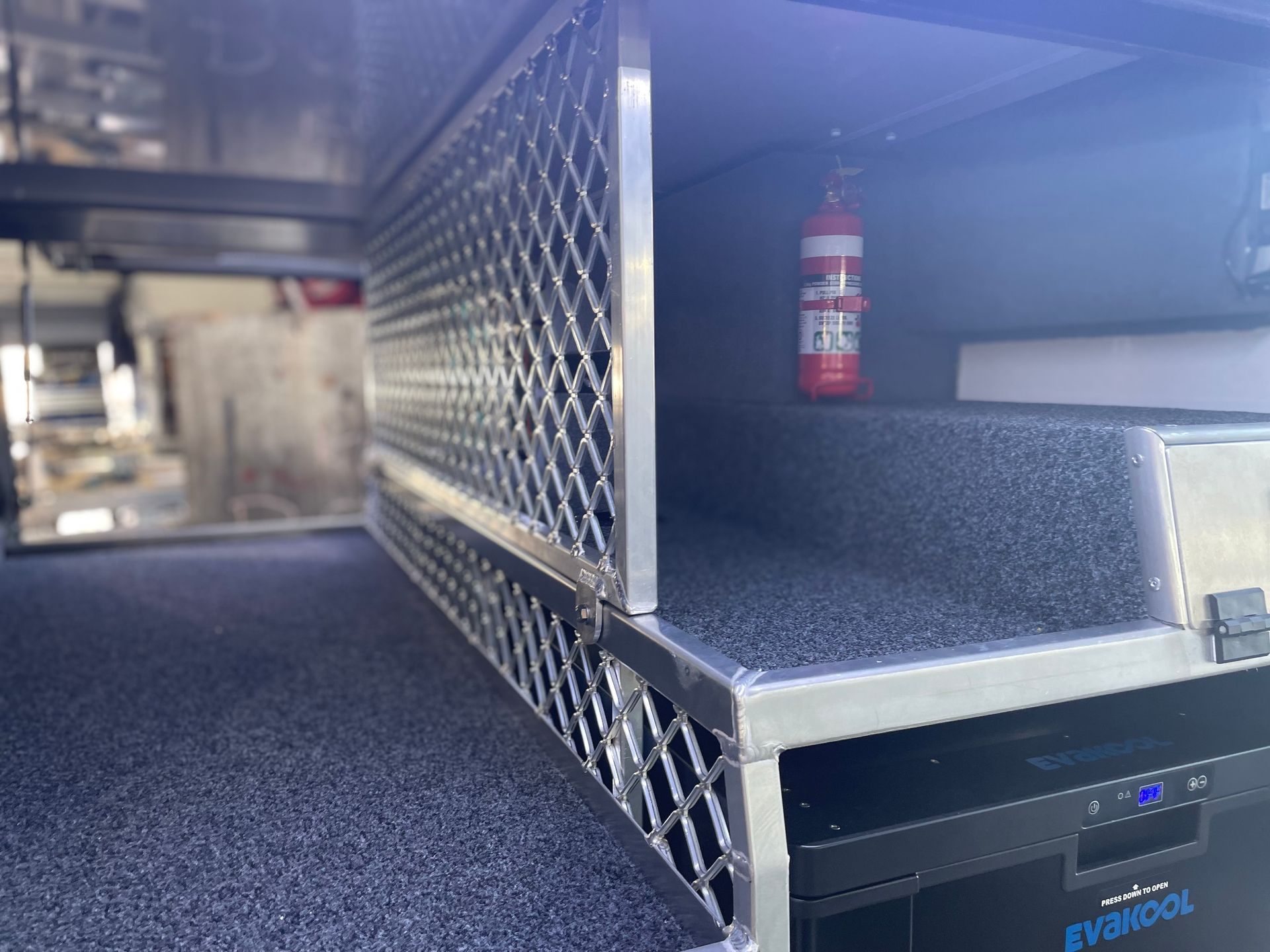 Compartment with metal mesh door, holding a fire extinguisher. Inside, a black storage platform. — Boyd's Fabrications In Portsmith, QLD