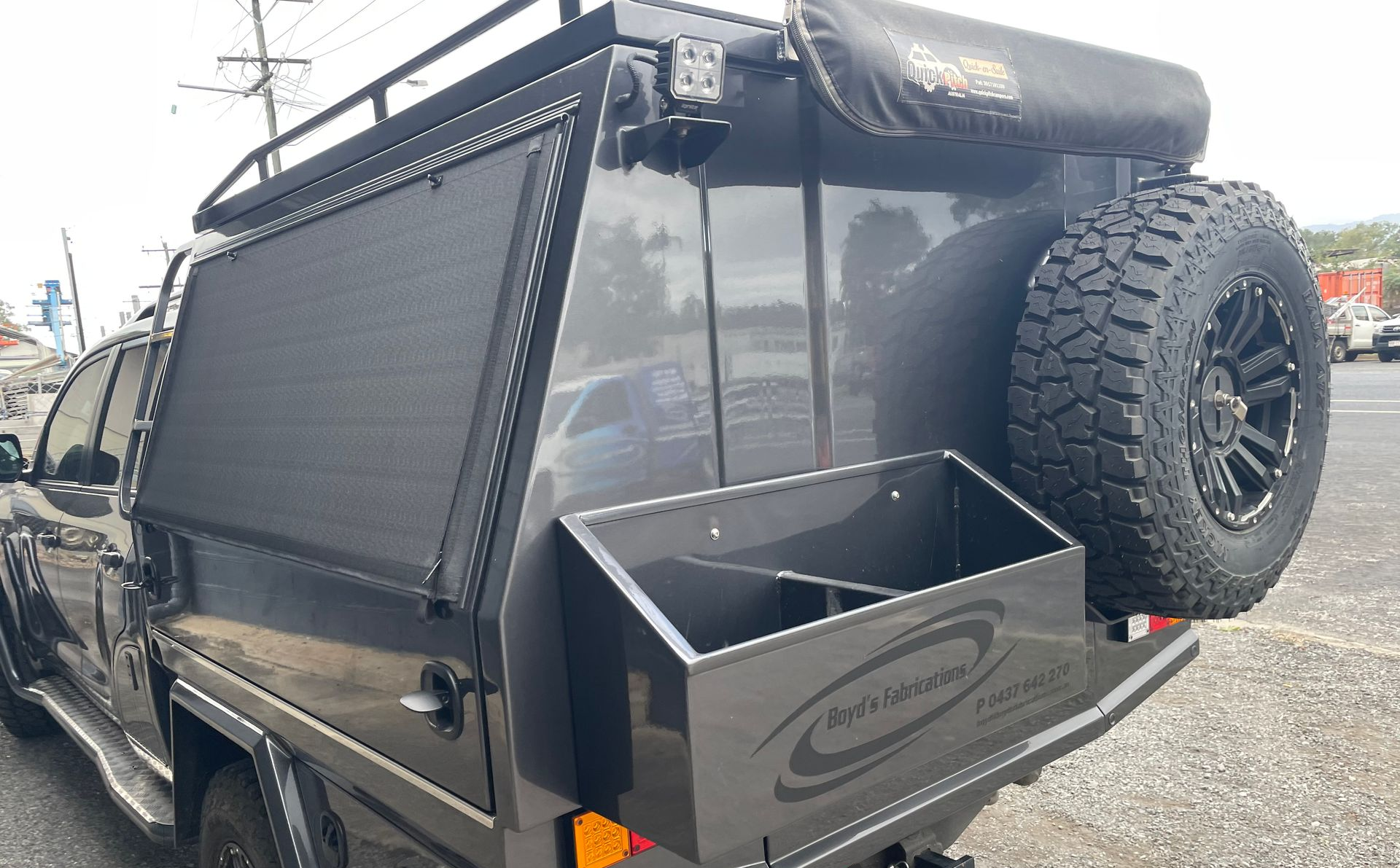 Grey truck bed with spare tire, storage box, and awning in parking lot.— Boyd's Fabrications In Portsmith, QLD 