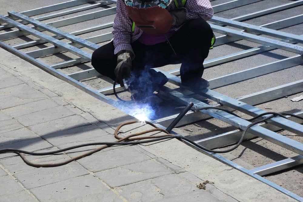 A Man is Welding a Metal Structure on the Ground — Boyd's Fabrications In Smithfield, QLD