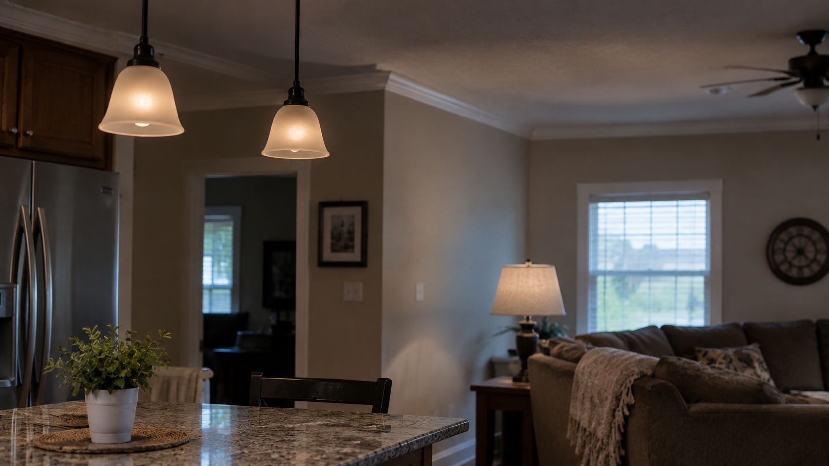 Cozy open-concept living room and kitchen with granite island, pendant lights, couch, lamp, and window.