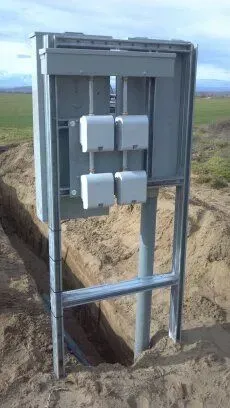 A large metal box is sitting in the middle of a dirt field.