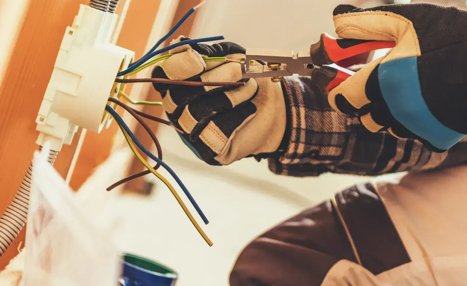 Hands connecting electrical wires to a white wall outlet during installation