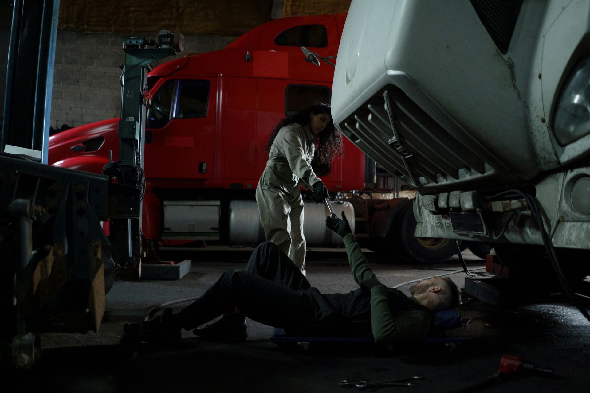 A man and a woman are working on a semi truck in a garage.
