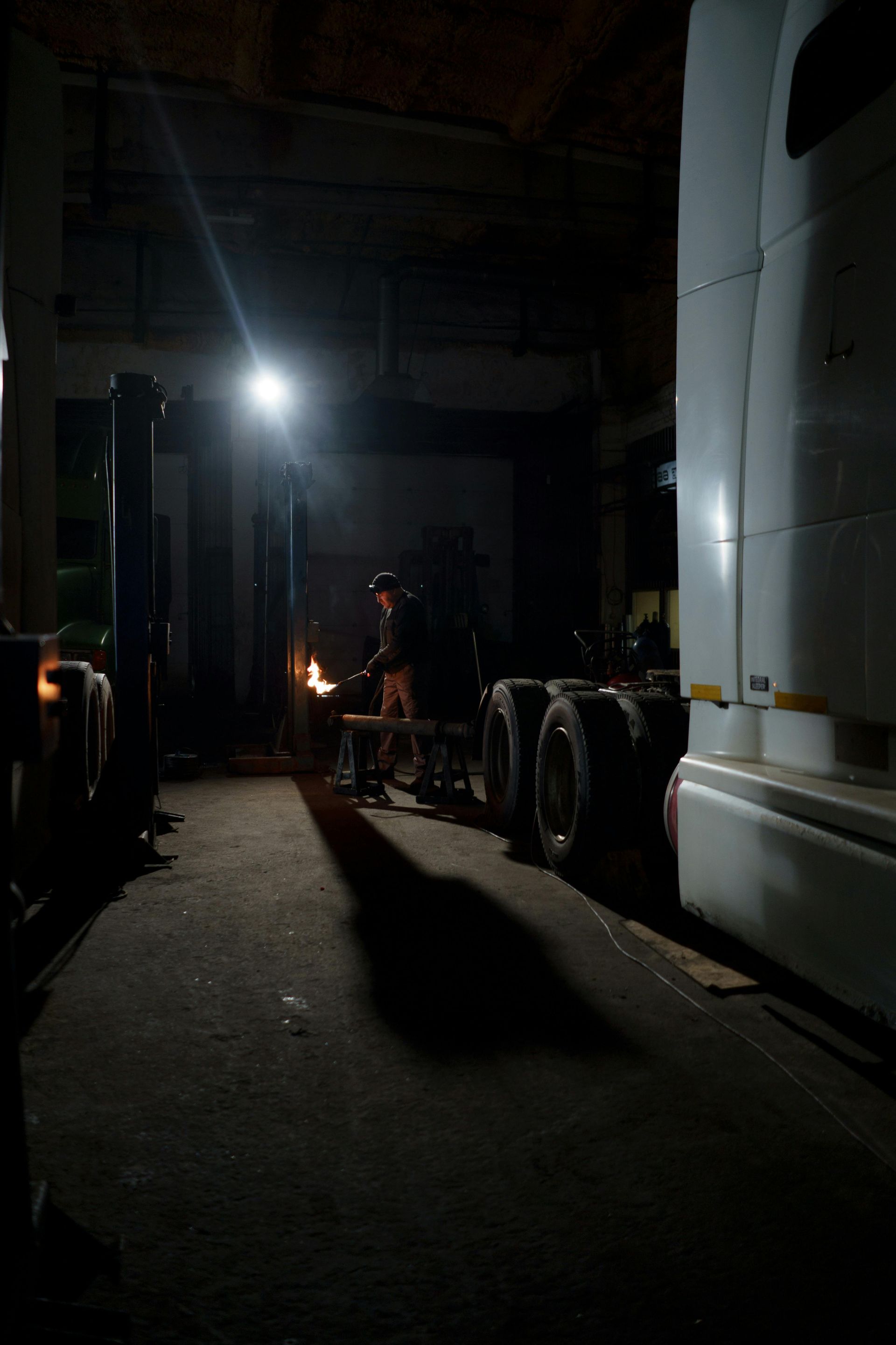 Dark alley beside trucks with a bright light and a person working in the distance