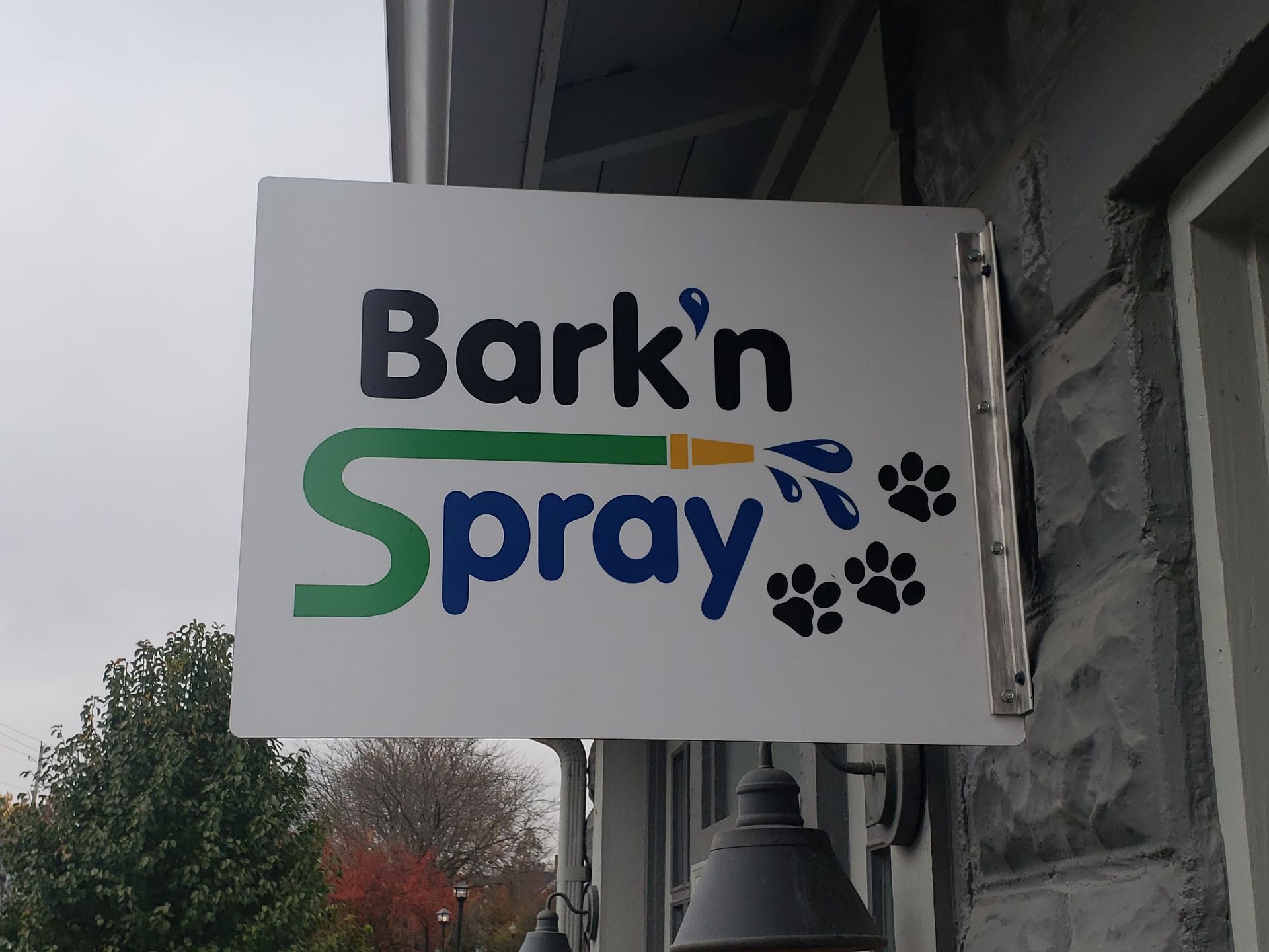Sign for Bark'n Spray pet grooming business, with blue and green text, a hose illustration, and paw prints on a white background.