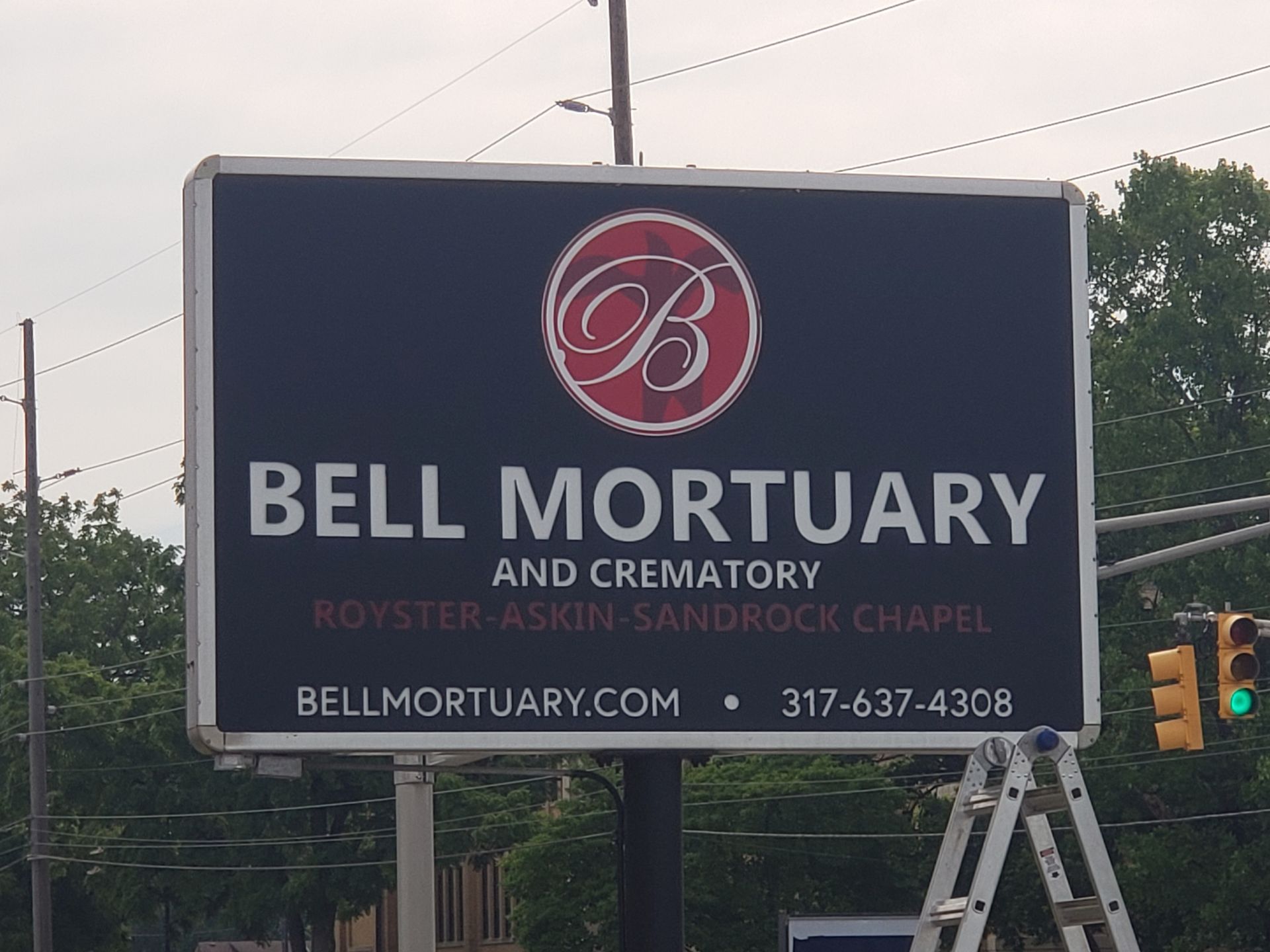 Sign for Bell Mortuary and Crematory. Dark blue background with white text, red logo. Includes website and phone number.