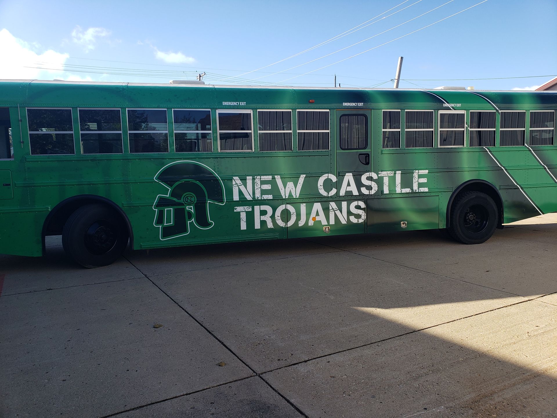 Green school bus with "New Castle Trojans" logo.