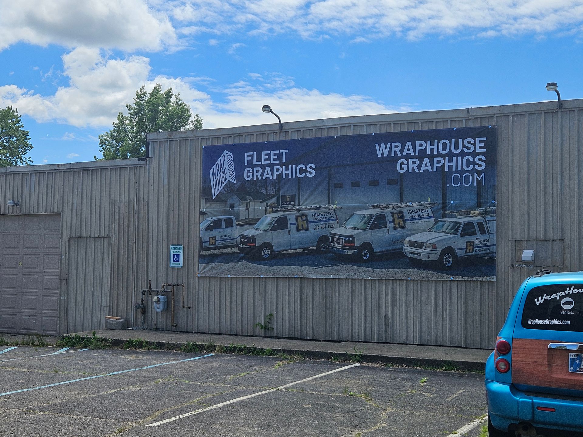 Fleet Graphics building with large sign featuring vans and website address. Parking lot, blue sky.