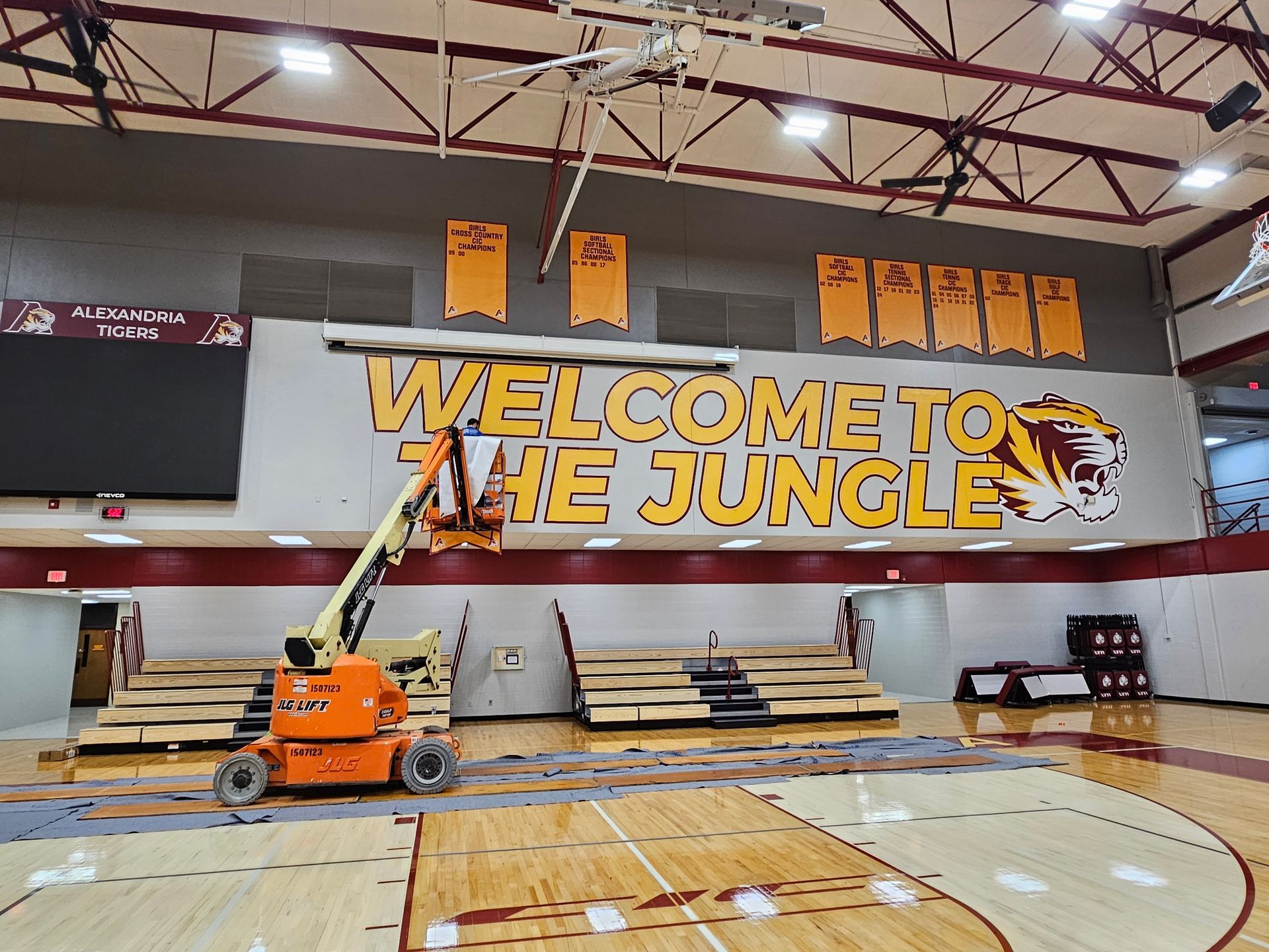 Gymnasium with "WELCOME TO THE JUNGLE" banner, bleachers, lift, and banners.