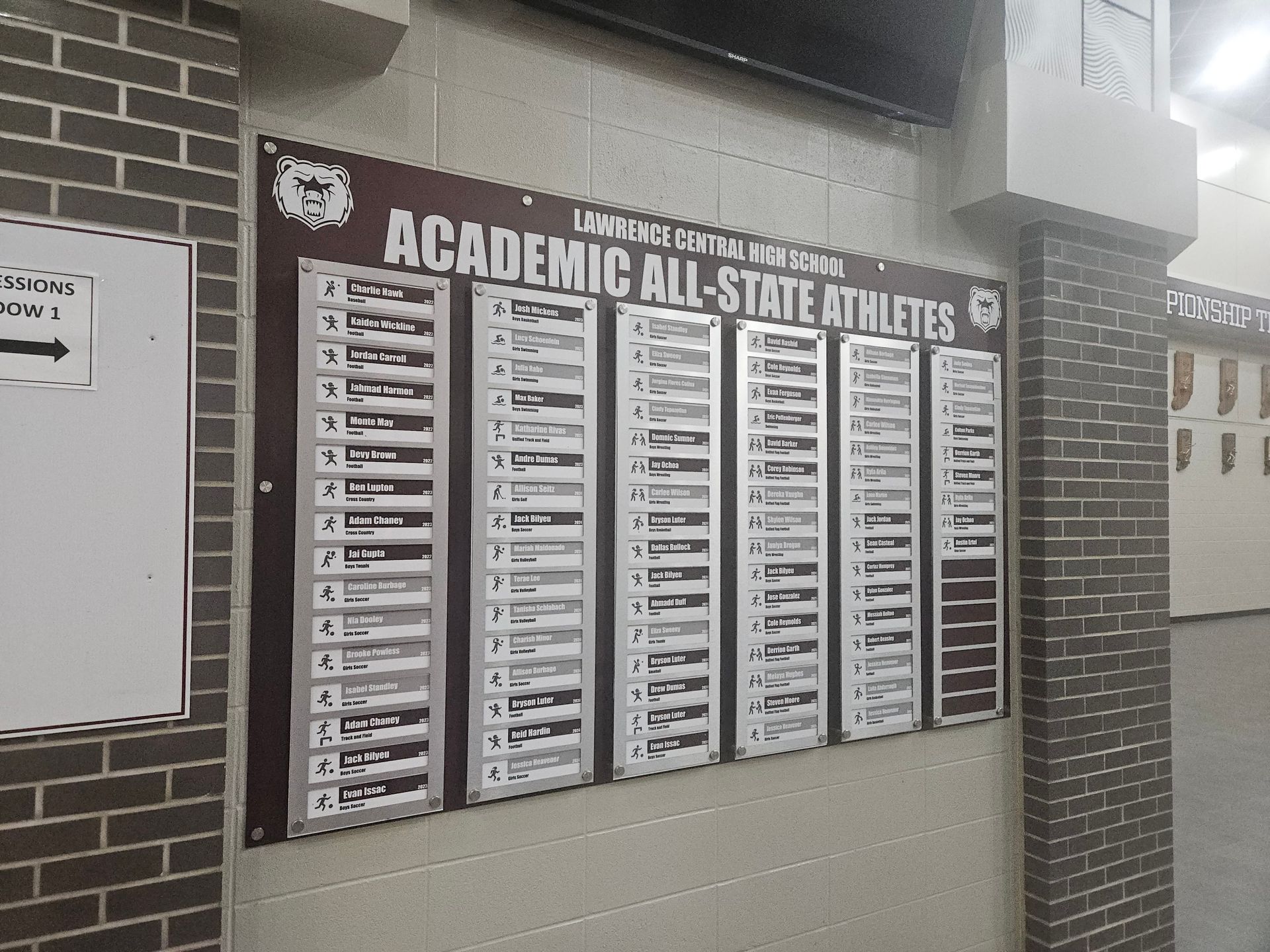 A wall display listing academic all-state athletes, likely in a school hallway. Text is white on a dark background.