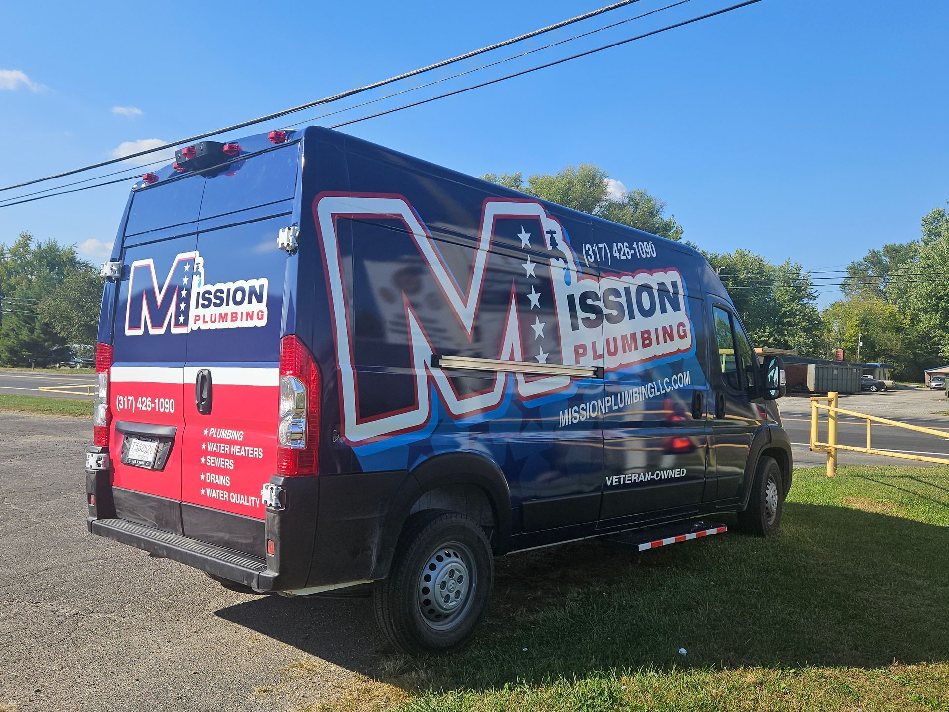 Blue and red Mission Plumbing van parked on a grassy area, displaying company logo and contact information.