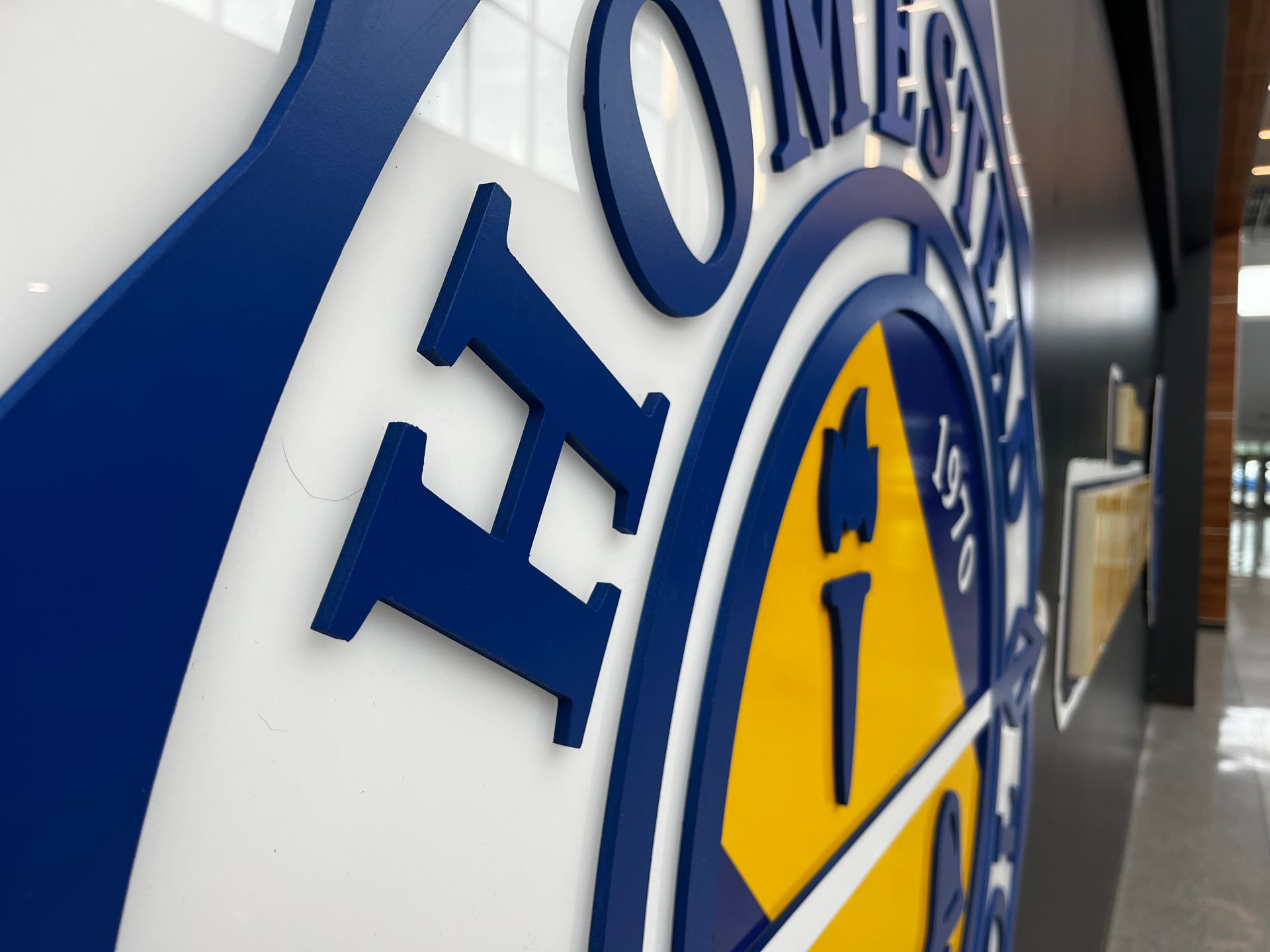 Close-up of a blue and gold school logo on a white wall. The logo includes the letter