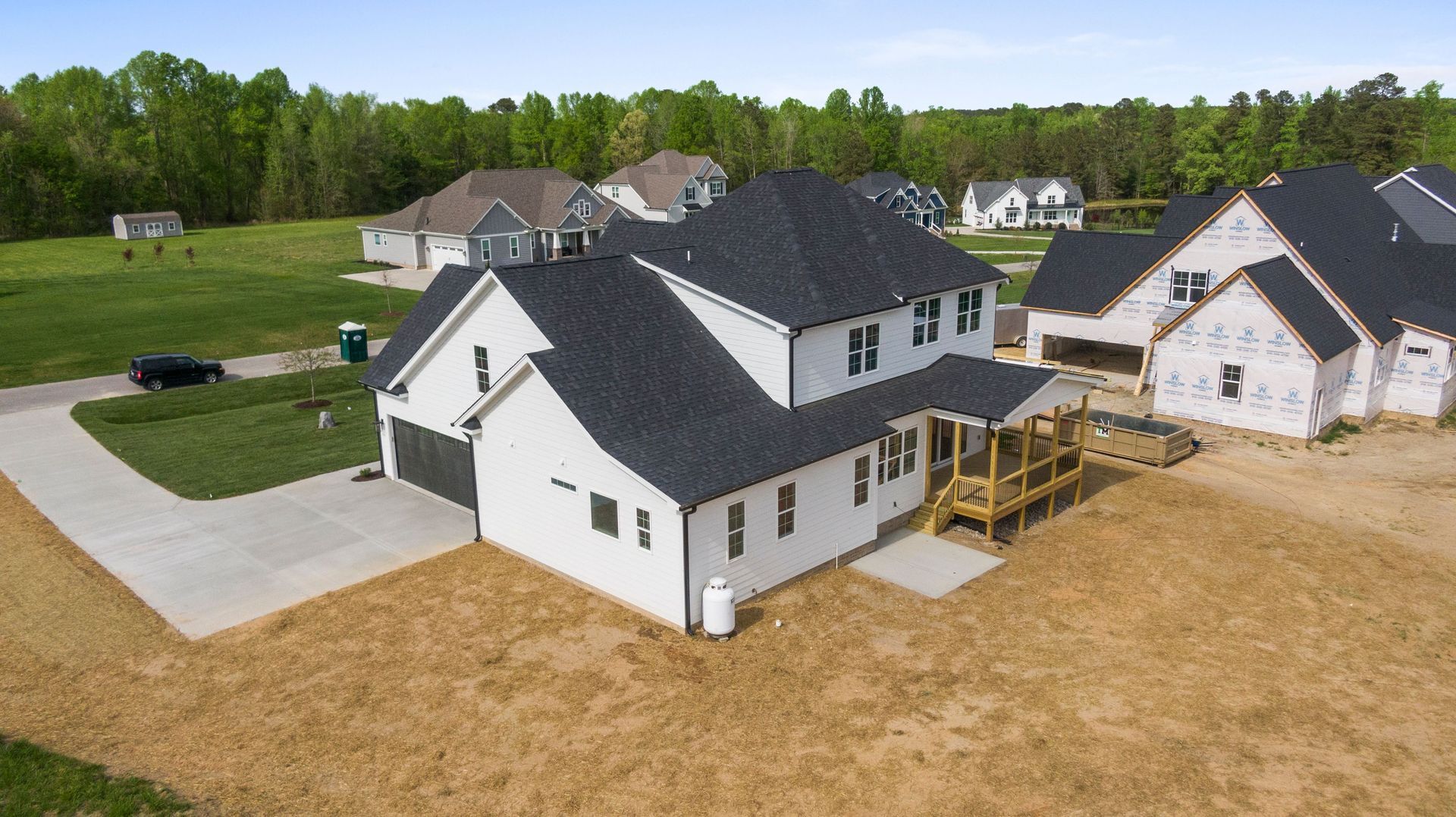 Aerial view of a new white house with gray roof and wooden deck in a suburban neighborhood