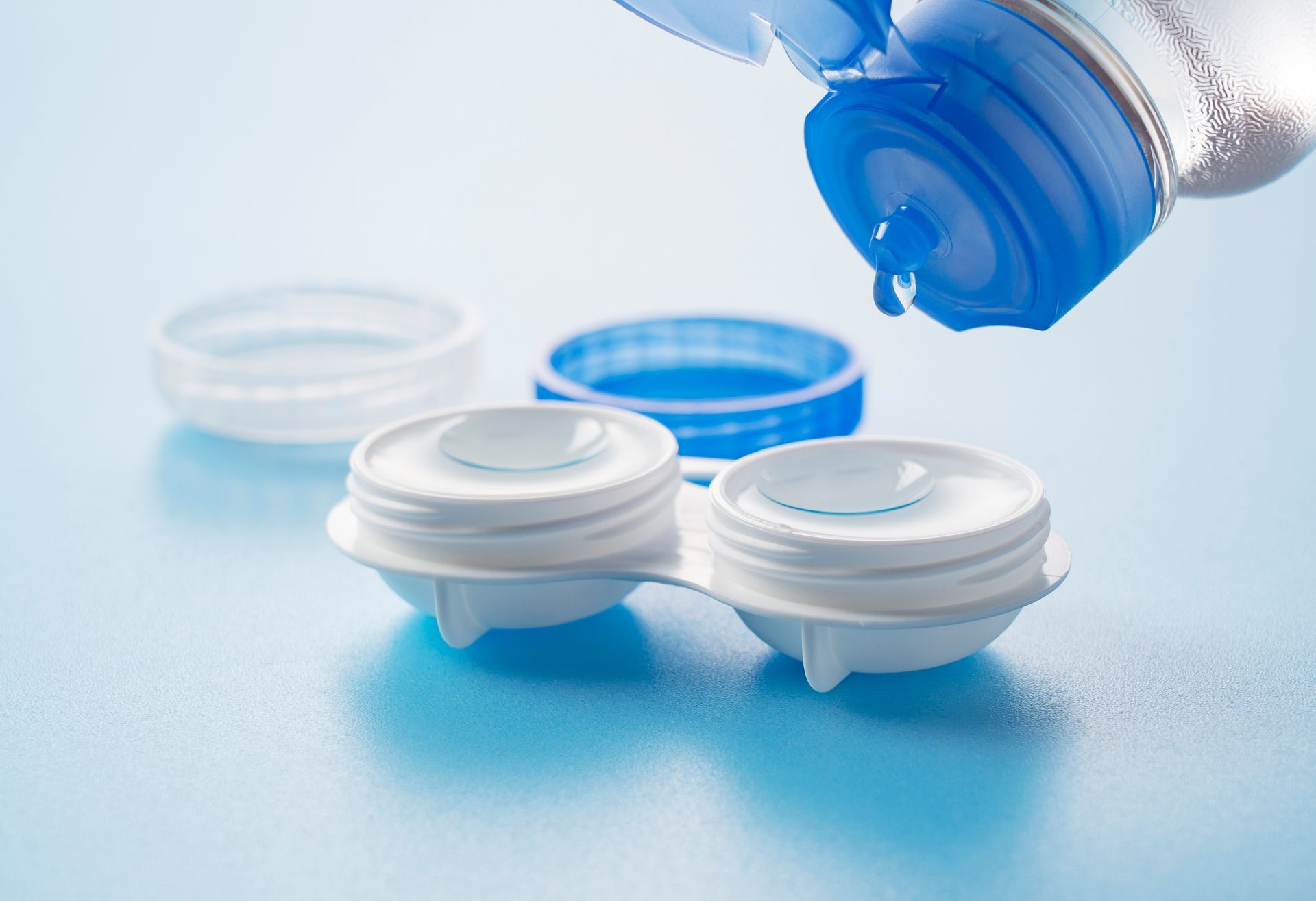 A bottle of contact lens solution is being poured into a contact lens case.