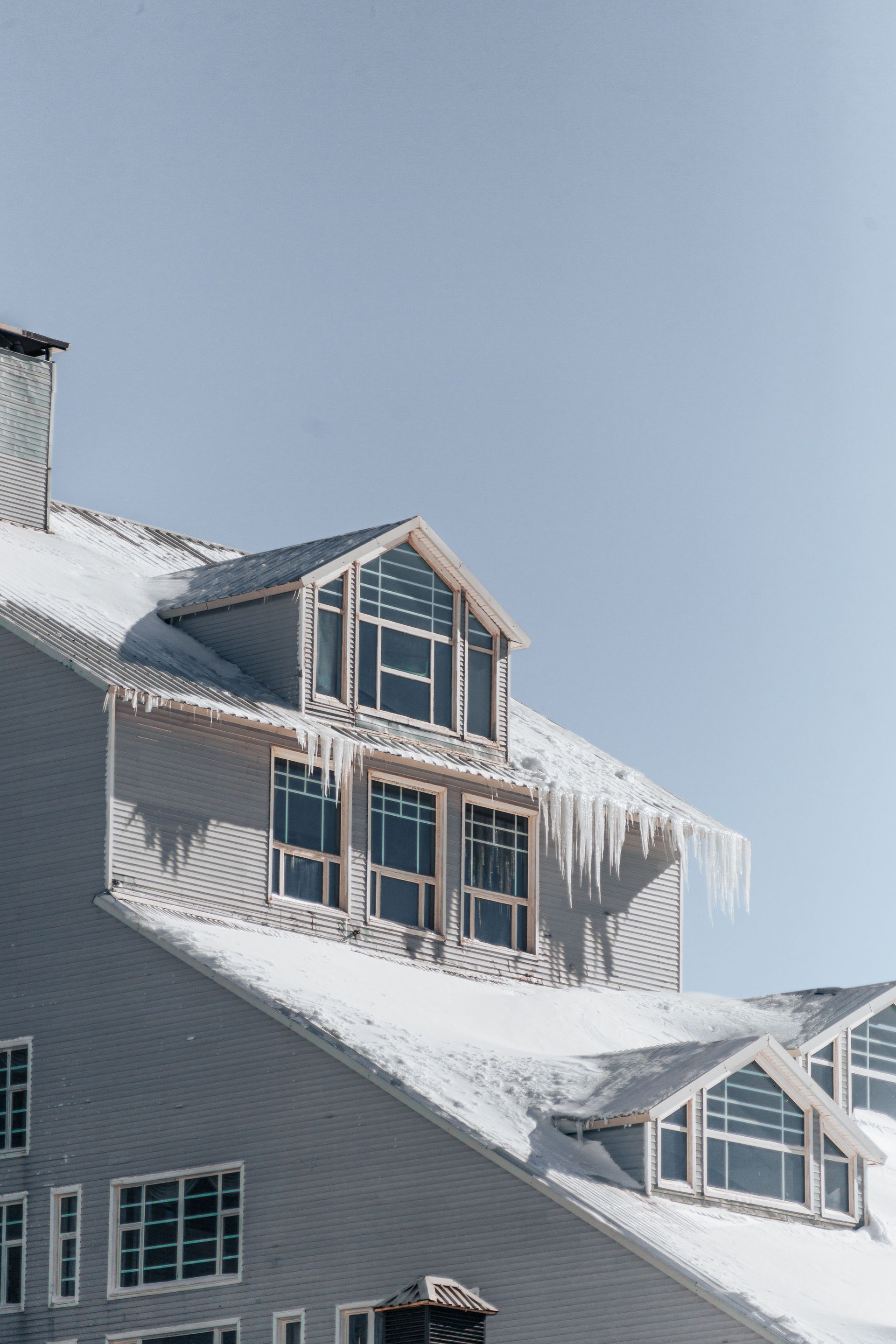 Snow-covered house roof with dormer windows under a clear blue sky