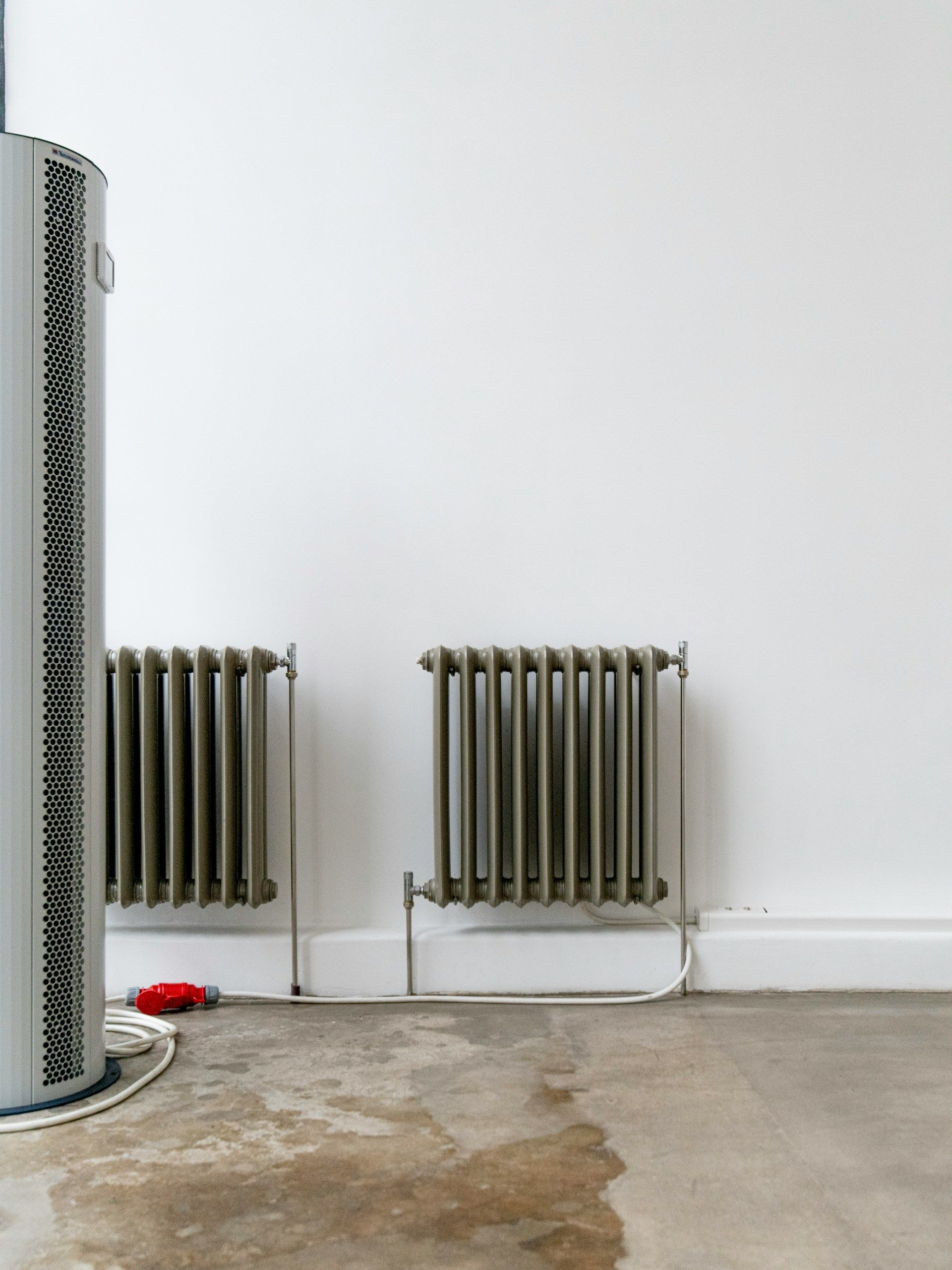 Two small radiators on a white wall beside a rough concrete floor and a silver column