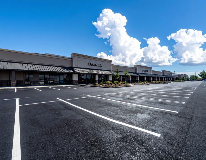 Empty parking lot in front of a strip mall with blue sky and puffy clouds.