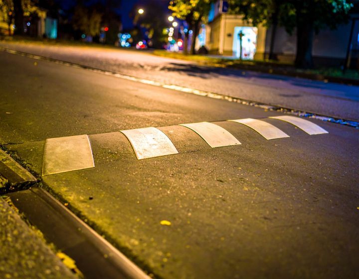 Speed bump on an asphalt road at night, painted with white stripes.