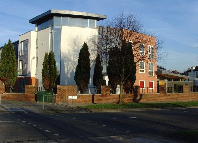 Brick apartment building with three stories and white-framed windows, benches, and lampposts on a sunny day.