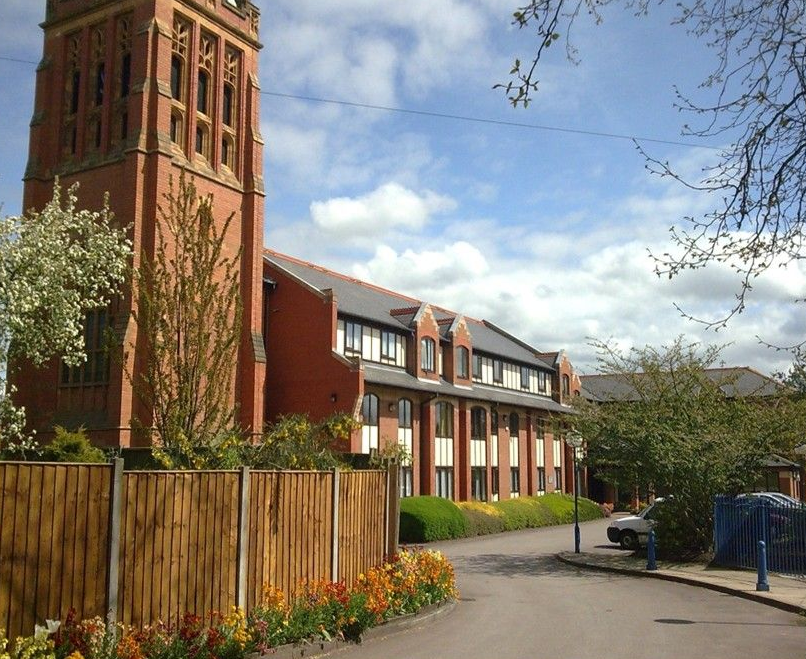 Brick apartment building with benches on a grassy lawn.