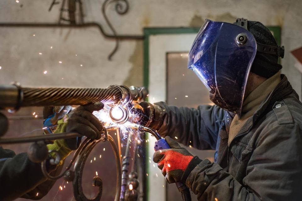 man is welding a piece of metal in a factory.