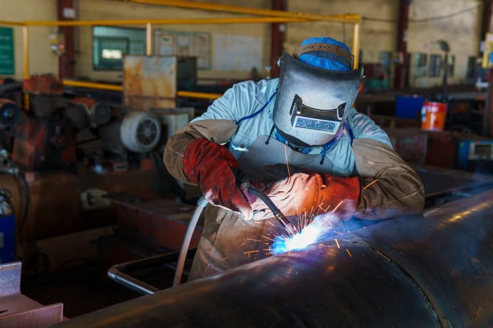 A man is welding a pipe in a factory.