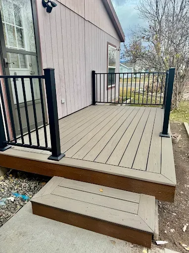 A beige composite deck with black metal railings and a single matching step leading up from a concrete walkway.