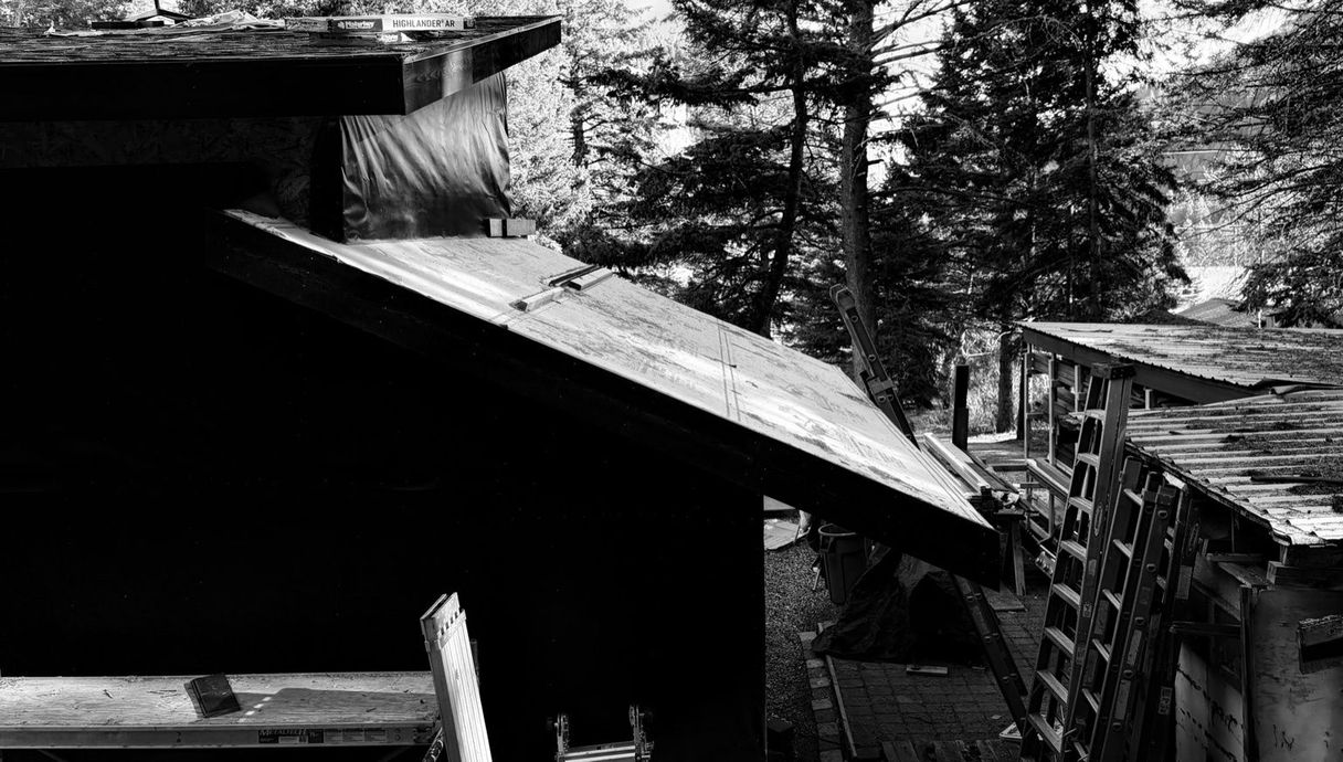 A wooden cabin with a large deck and ground-level hot tub nestled in a snowy, pine-covered forest.