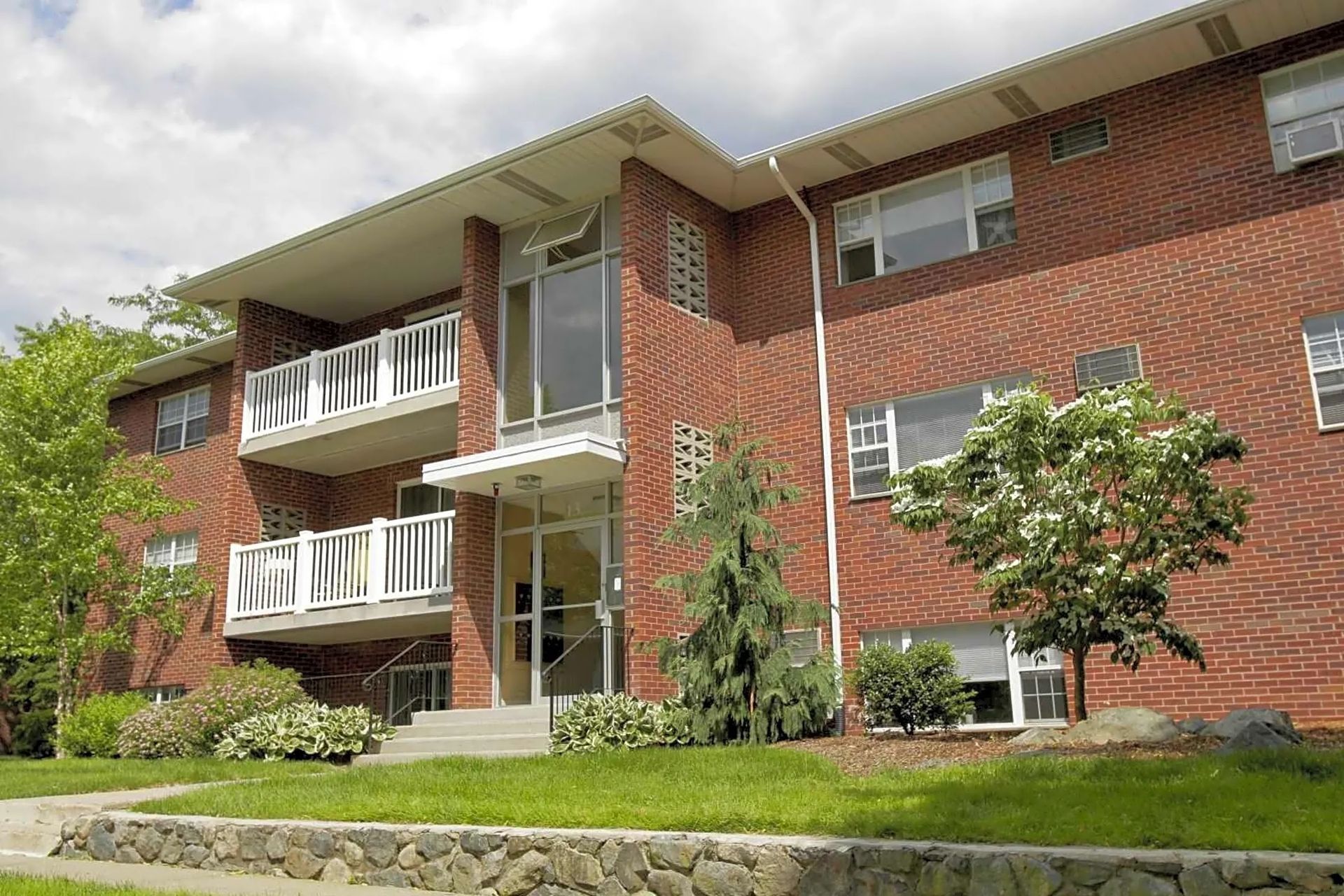 Exterior of brick apartment building with balconies and landscaped grounds at Waltham Overlook Apartments in Waltham, MA.