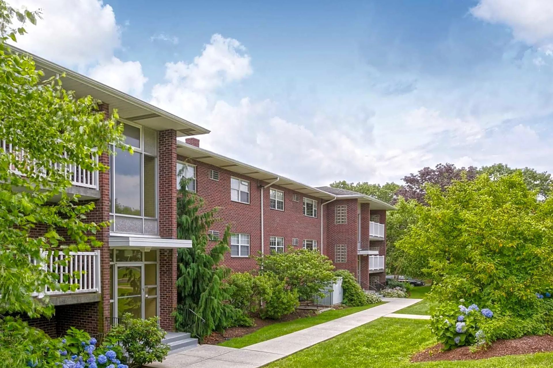 Brick apartment building surrounded by trees and landscaped grounds at Waltham Overlook Apartments in Waltham, MA.
