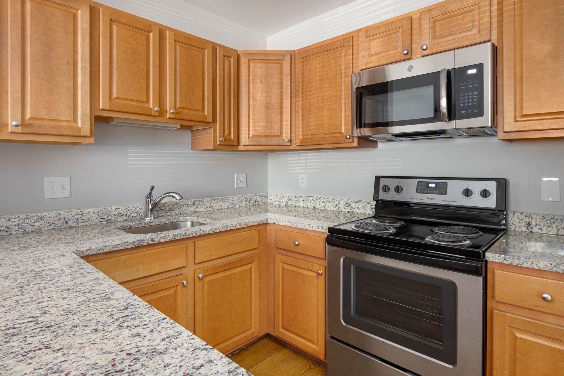 Kitchen with wood cabinets, granite countertops, microwave, and stove at Waltham Overlook Apartments in Waltham, MA.