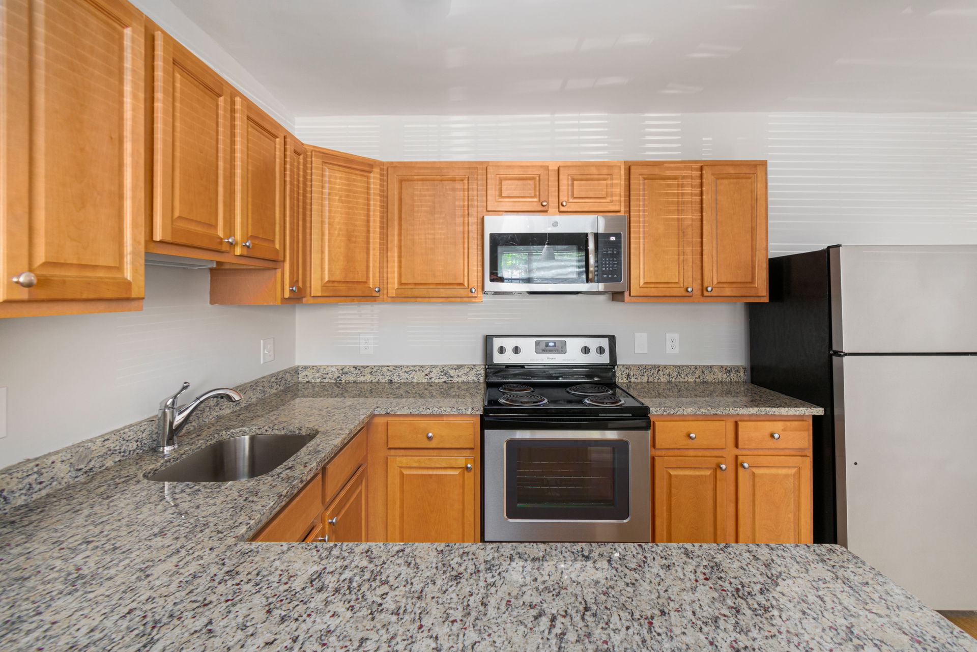 Apartment kitchen with granite countertops, wood cabinets, and appliances at Waltham Overlook Apartments in Waltham, MA.