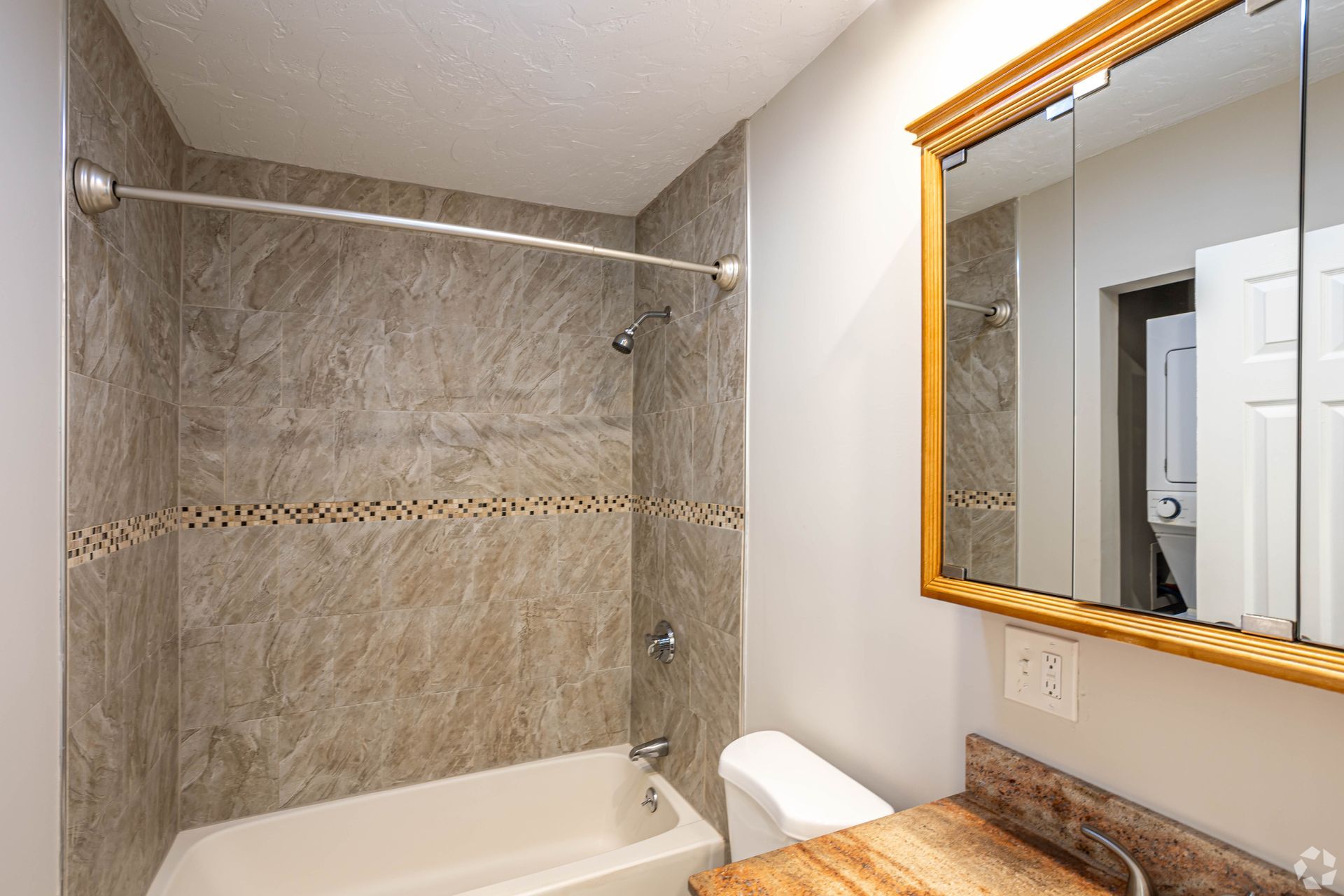 Bathroom with bathtub, tiled shower surround, and vanity mirror at Waltham Overlook Apartments in Waltham, MA.