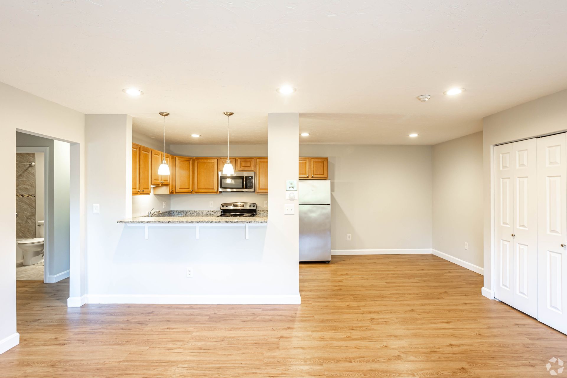 Open-concept apartment interior with kitchen, breakfast bar, and wood-style flooring at Waltham Overlook Apartments in Waltham, MA.