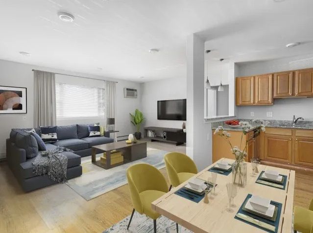 A picture took from the dining room area overlooking the living room with dining set, sofa, TV, and oversized window at Waltham Overlook Apartments in Waltham, MA.