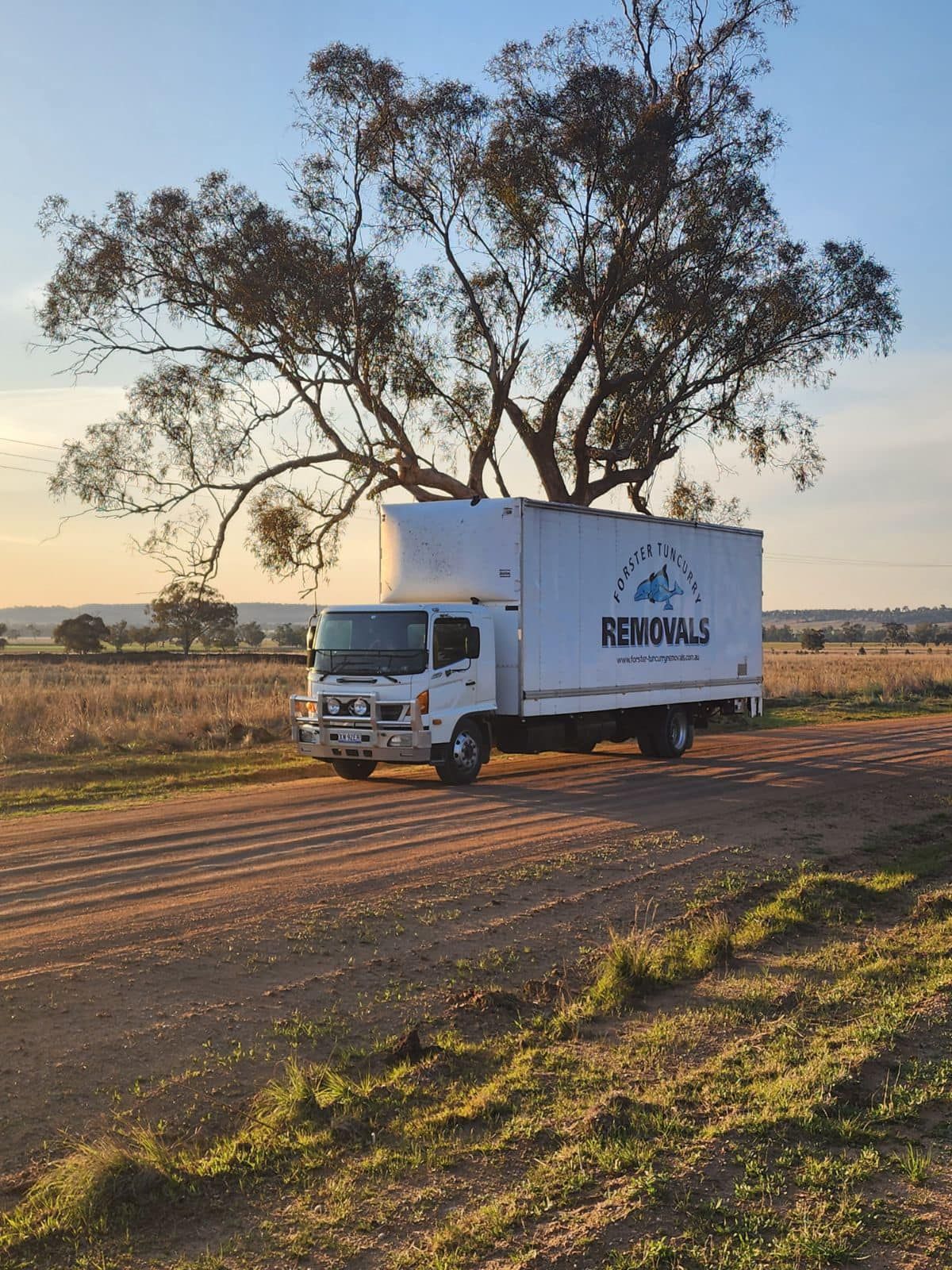 A Moving Truck is Parked on the Side of a Dirt Road Next to a Tree — Forster Tuncurry Removals & Storage in Gloucester, NSW
