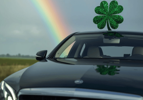 Black car parked near an open field with a rainbow behind it and a shamrock decoration on the roof.