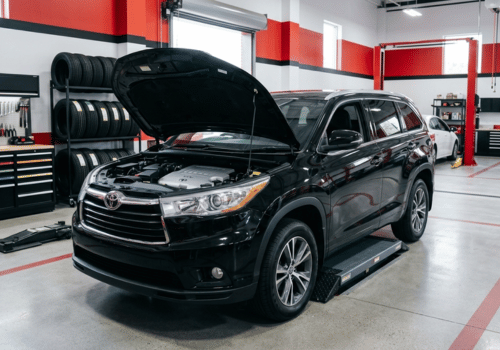 Black Toyota Highlander SUV inside a clean, modern auto repair shop with the hood open