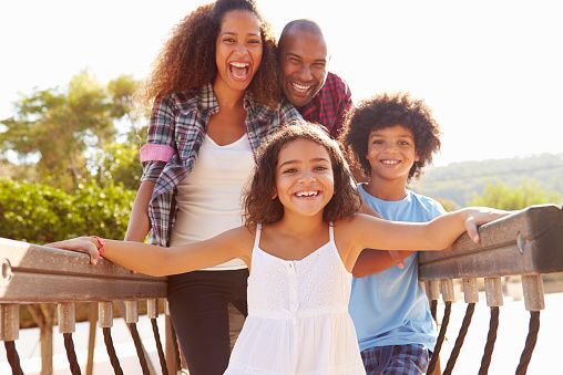 Four smiling people leaning on a wooden bridge outdoors in bright sunlight