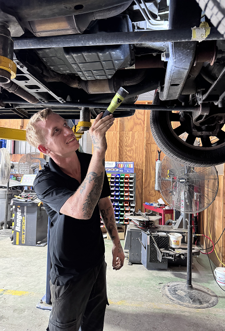 Mechanic inspecting the underside of a car on a lift in an auto repair shop | JB Auto Works