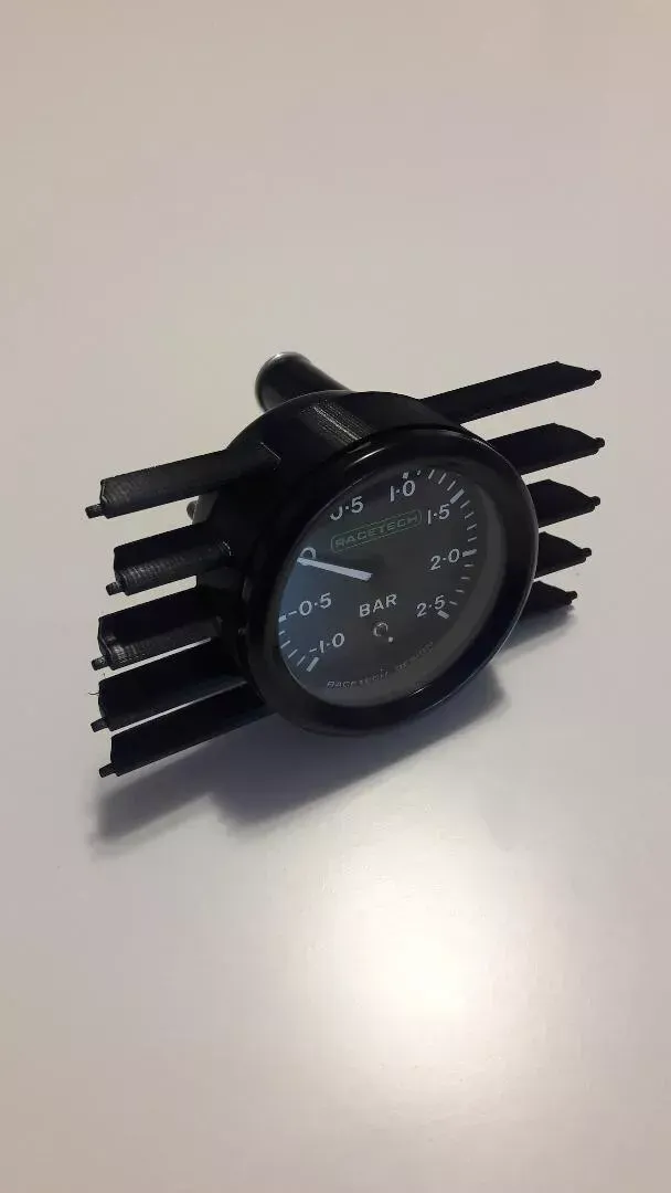 Black gauge with fins, likely for a vehicle, showing a reading against a white backdrop.