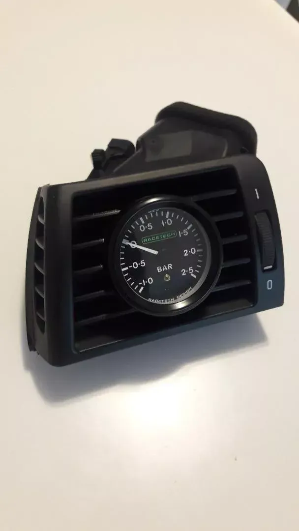 Black car air vent with a circular gauge installed.