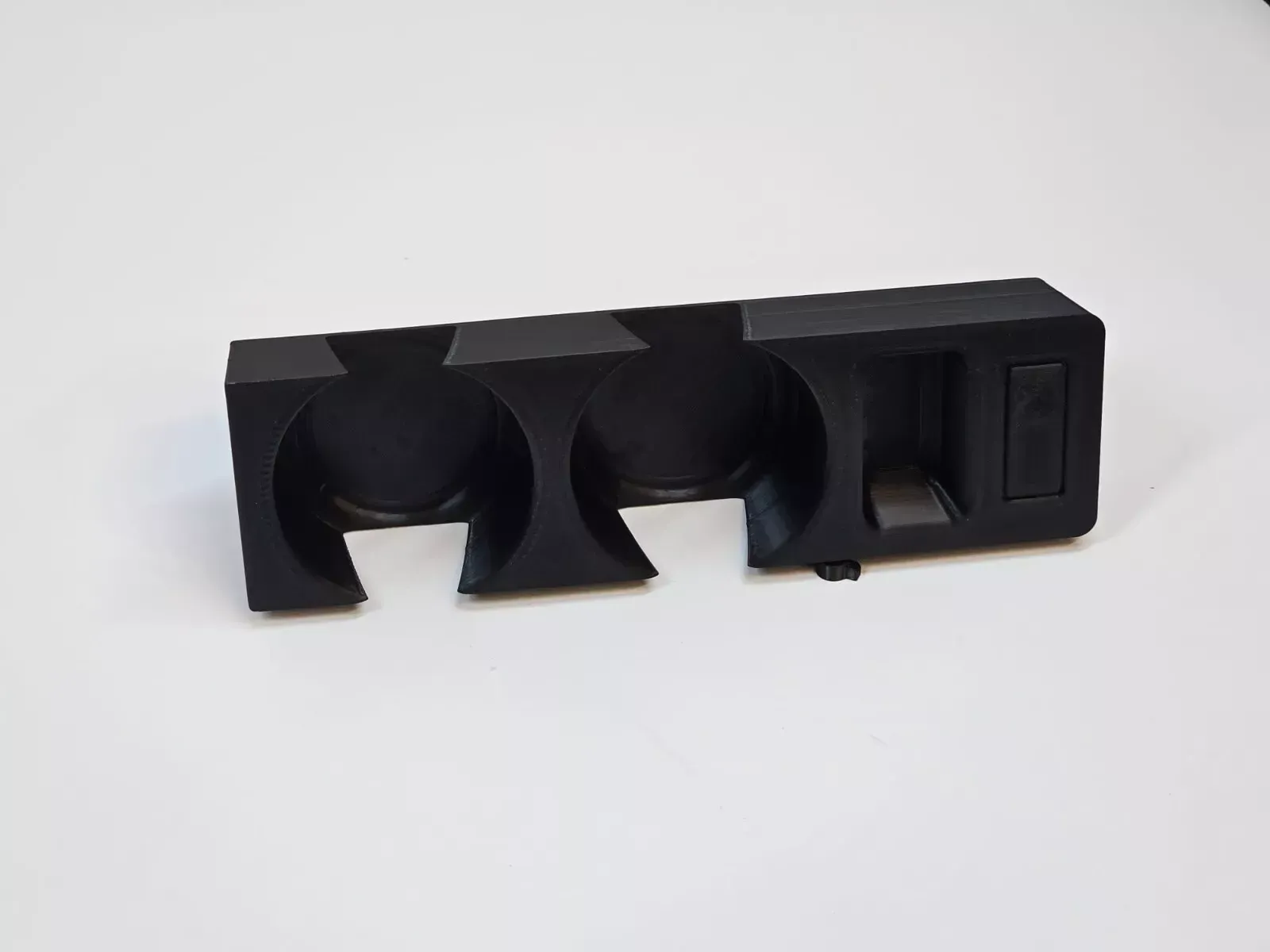 Black plastic car console with two cup holders and a small storage area.