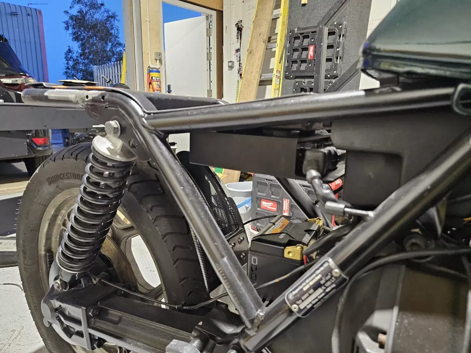 Motorcycle frame with black metal and rear suspension, inside a workshop.