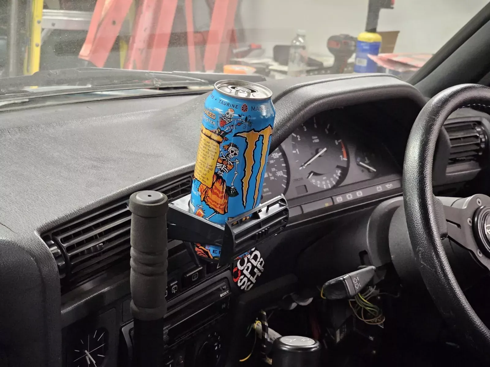 A Monster energy drink can in a custom-built car cup holder on a car dashboard.