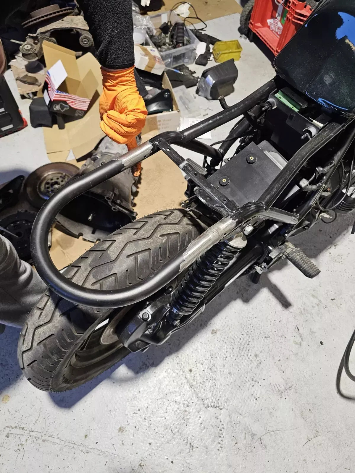 A person with orange gloves working on a motorcycle frame in a garage.