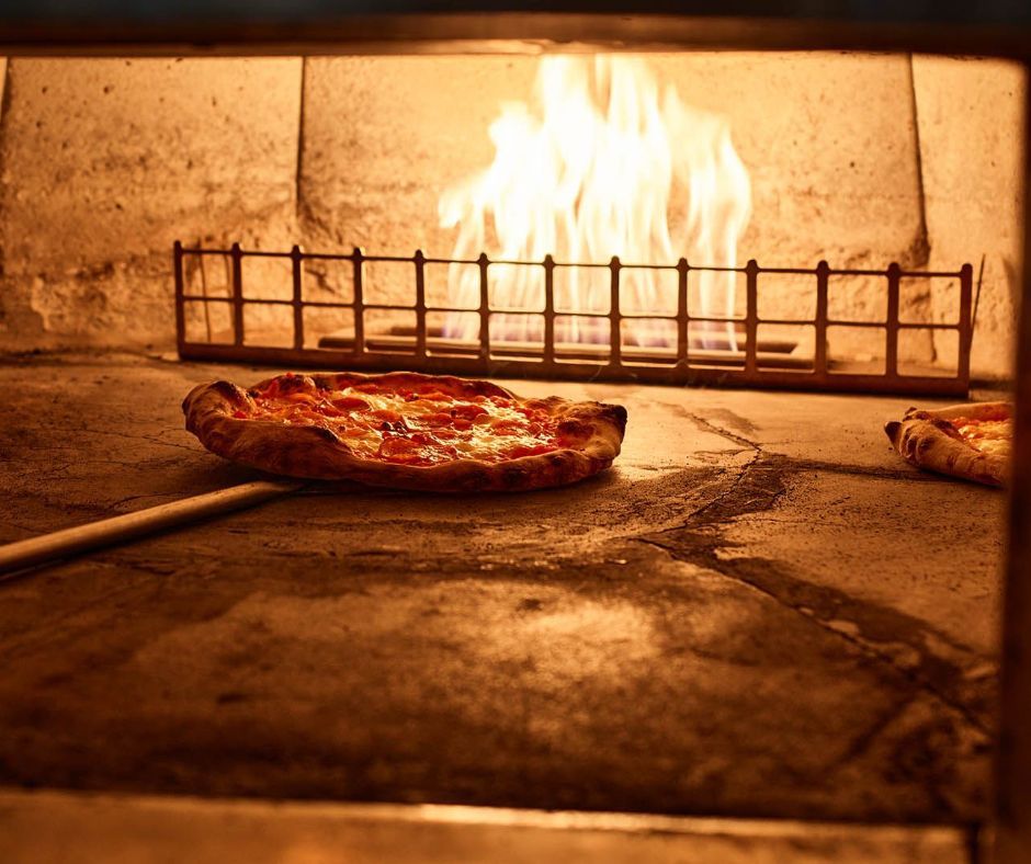 A pizza is being cooked in a wood fired oven