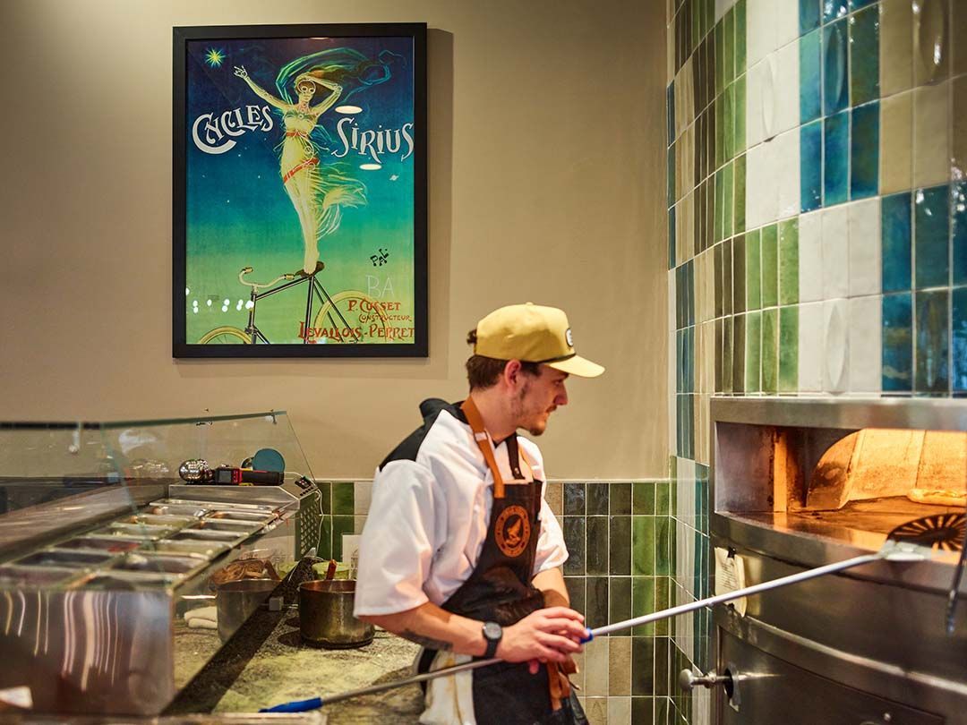 A man is standing in front of a pizza oven in a kitchen.